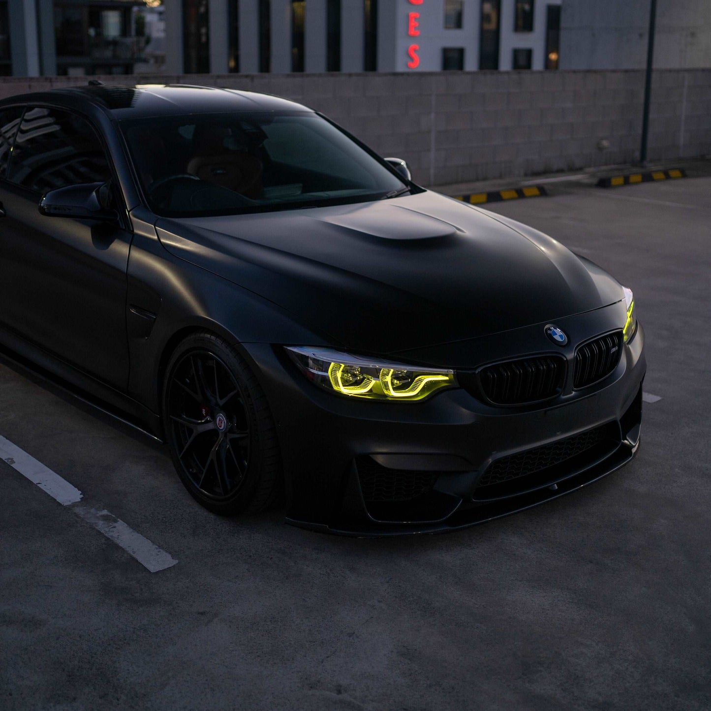 Black BMW car with glowing yellow headlights in a parking lot.