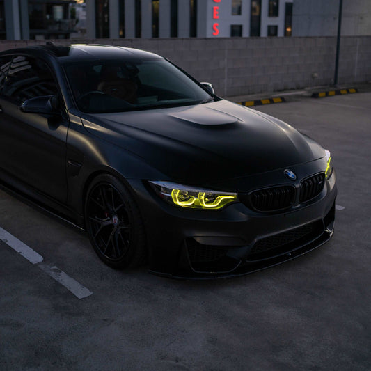 Black BMW car with glowing yellow headlights in a parking lot.